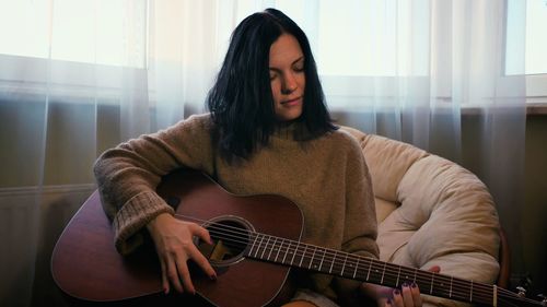 Young woman playing guitar while sitting on sofa at home