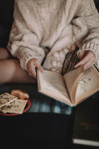 Cropped young woman in a cozy knitted sweater reading a book on the bed. home aesthetics. winter