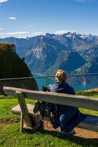 Rear view of man sitting on railing against mountain