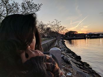 Close-up of mid adult woman standing by lake against sky during sunset