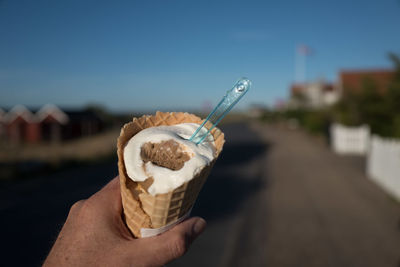 Close-up of hand holding ice cream cone against sky