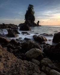 Rocks on beach against sky during sunset