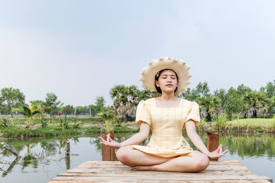 Woman practicing yoga and meditating in lotus position on wooden bridge.