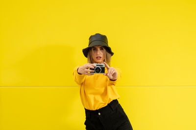 Close-up of a smiling young caucasian woman on a yellow background holding a photo camera