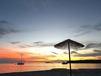 Silhouette sailboat on beach against sky during sunset