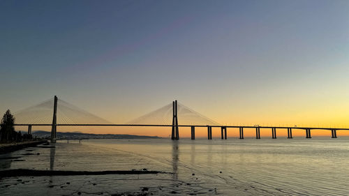Suspension bridge over sea against sky during sunrise