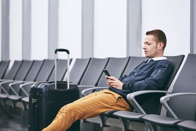 Man using mobile phone while sitting on chair at airport terminal