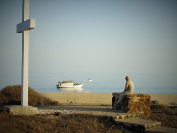 Man sitting on wall against clear sky