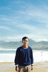 Portrait of young man standing at beach against sky