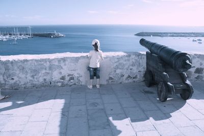Girl and canon by retaining wall against sea