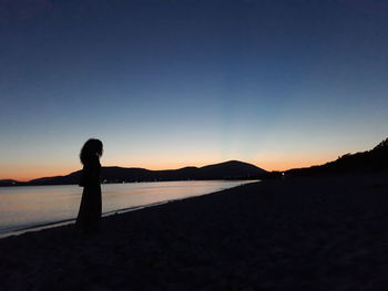 Silhouette woman standing on beach against sky during sunset