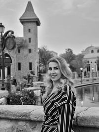 Portrait of young woman standing against built structures