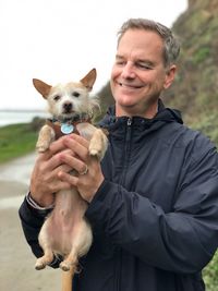 Smiling mature man holding dog while standing on road