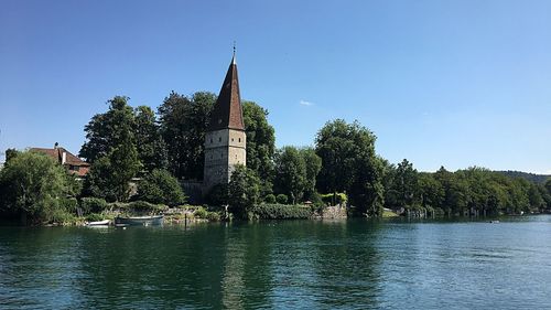 Trees by river against building against clear sky