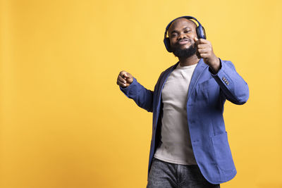 Young man using mobile phone while standing against yellow background