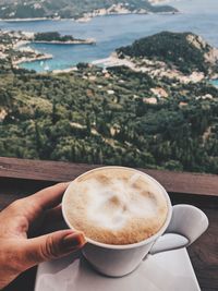 Cropped hand of woman having coffee at table against sea