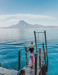 Man on wooden post by pier against sky