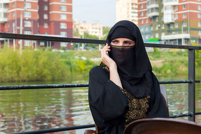 Muslim woman speaks on a smartphone on the background of the river and the city.