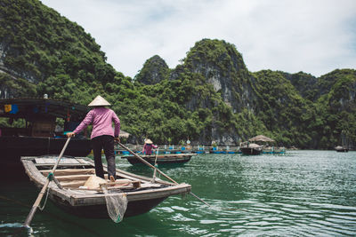 Rear view of woman standing in rowboat on halong bay by mountains