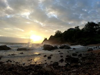 Rocks on beach against sky during sunset