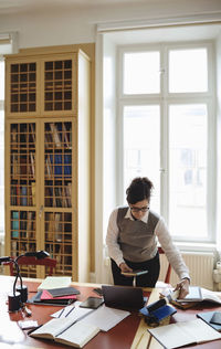 Female lawyer holding book while standing at table in library
