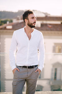 Young man looking away while standing against building