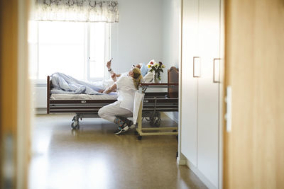 Female nurse and senior man taking selfie with smart phone in hospital ward