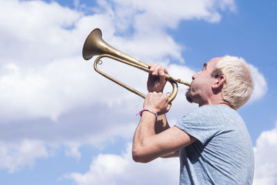 Low angle view of man playing trumpet against sky