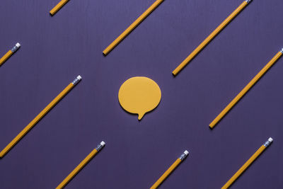 Close-up of yellow pencils and speech bubbles on purple table