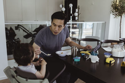 Father feeding male toddler over table at home