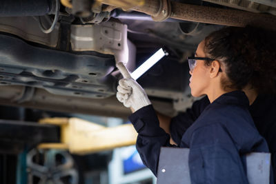 Woman pointing at car engine at auto repair shop