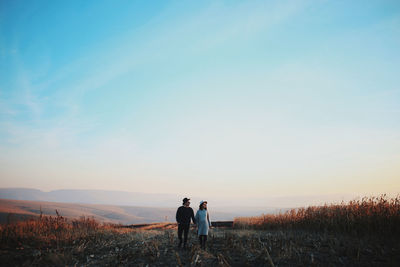 Rear view of man walking on field against sky during sunset