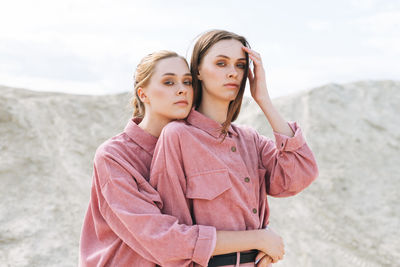 Fashion beauty portrait of young women sisters in pink organic velvet shirts on desert background