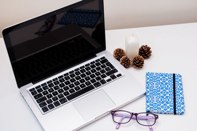 High angle view of laptop with book and eyeglasses on table against white background