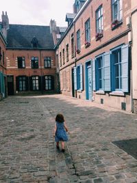 Full length rear view of girl walking on cobblestone street in city