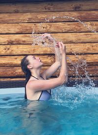 Side view of young woman splashing water in swimming pool