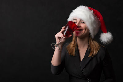 Portrait of young woman holding hat against black background