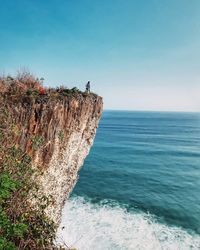 Man on rock by sea against clear blue sky