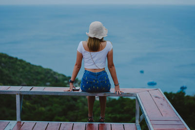 Rear view of woman standing by railing against sea