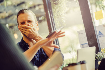 Businessman covering mouth while colleague balancing phone in office