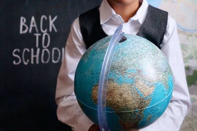 Midsection of man with globe against blackboard in classroom