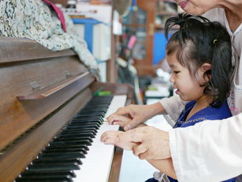 Midsection of grandmother assisting granddaughter in playing piano at home