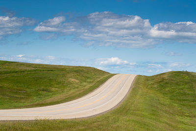 Empty road amidst field against sky