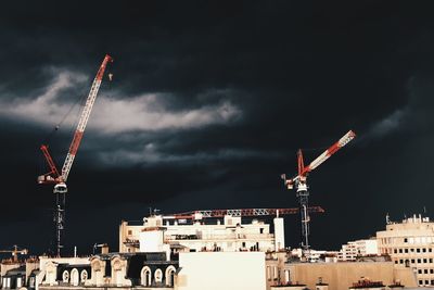 Cranes amidst buildings in city against sky