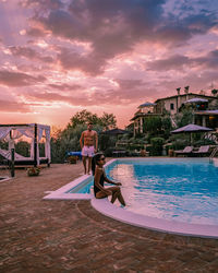 Couple by swimming pool against sky during sunset