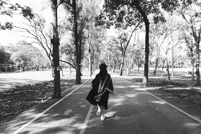 Rear view of woman running on road amidst trees