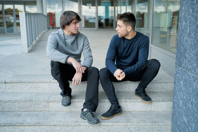 Front view of two young men talking sitting on a city staircase and