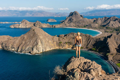 Man standing on rock by sea against sky