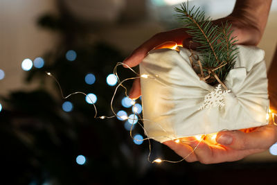 Cropped hands of person holding gift box with illuminated christmas lights