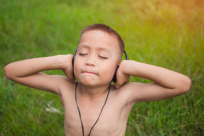 Shirtless boy with eyes closed listening music on grass